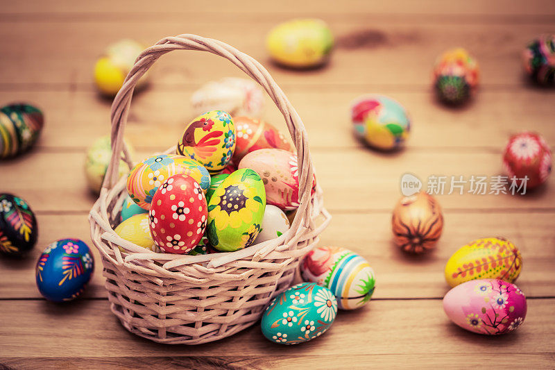 彩色的手绘复活节彩蛋在篮子和木头上。手工制作的装饰