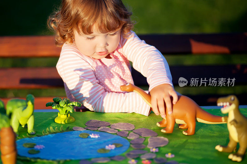 蹒跚学步的孩子在玩玩具恐龙。