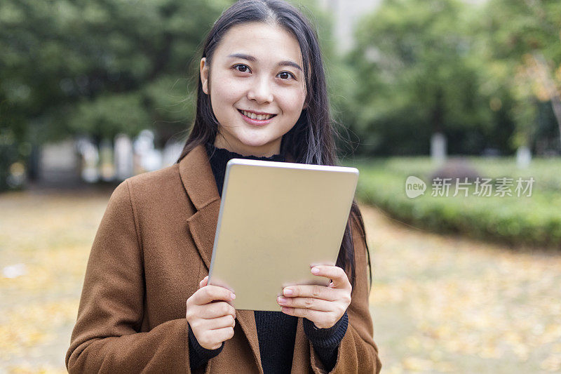 年轻的亚洲女子拿着平板电脑走在街上