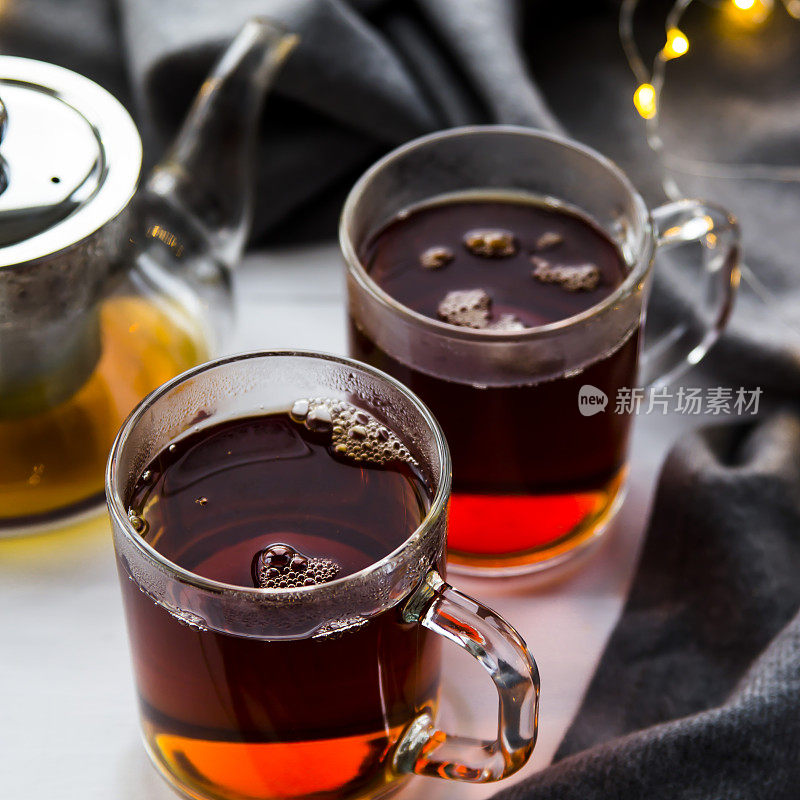 木桌上放着黑色透明茶壶和红茶杯，旁边是一条灰色围巾和灯。冬天家里的概念