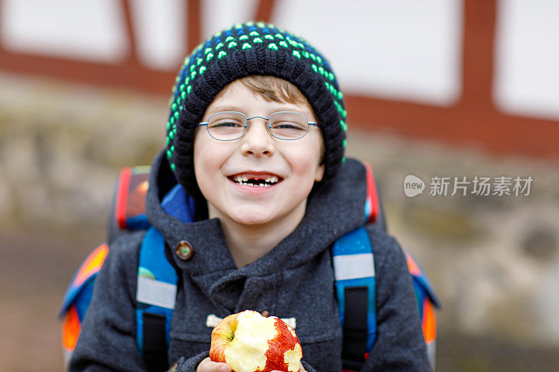 戴眼镜的小男孩从学校走出来，吃着苹果