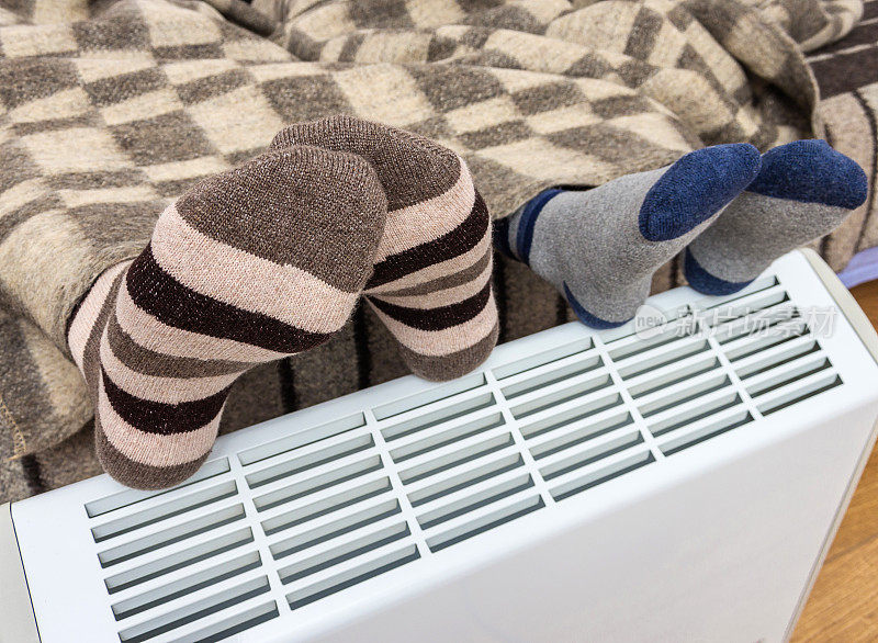女人和孩子在毛呢格子下面暖腿在电暖炉在家里冬天。