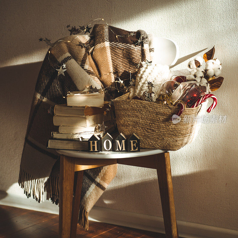 冬天暖和的毯子放在椅子上，上面放着一篮子圣诞装饰品、书和led串灯。首页冬天的阅读。房子