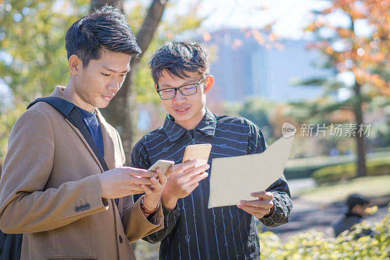 年轻的亚洲男子和日本朋友寻找旅游地点使用手机和花时间在亚洲旅行