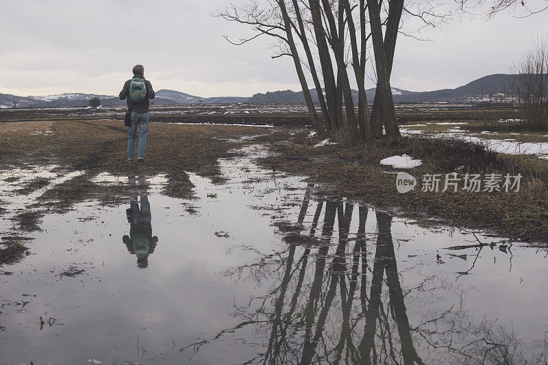 美丽快乐的成年人徒步旅行在潮湿的泥泞的田野在冬末