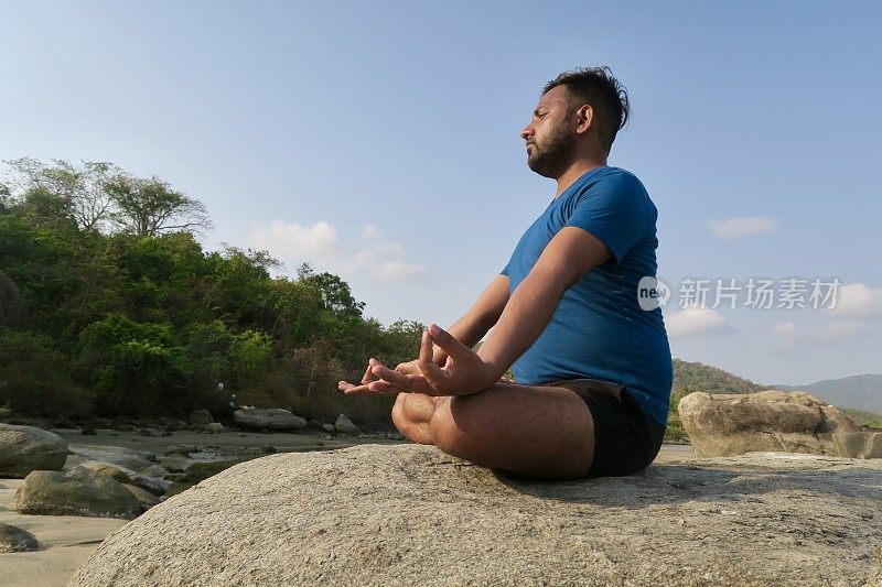 印度男子练习莲花姿势(莲花瑜伽)瑜伽位置在岩石，水的边缘，帕洛伦海滩，果阿，印度