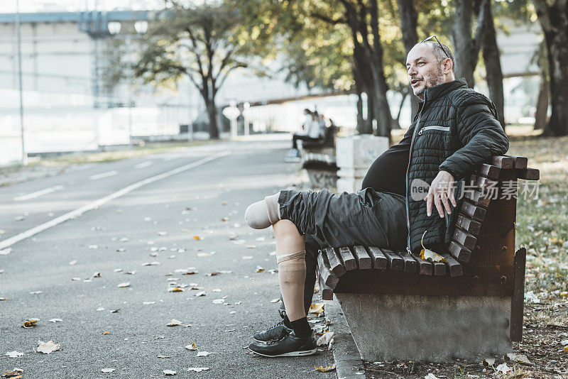 一个装着假腿的成熟男人正在城市公园的长椅上放松