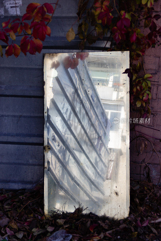 金属波纹篱笆的倒影在废弃的古董旧镜子靠在墙上。