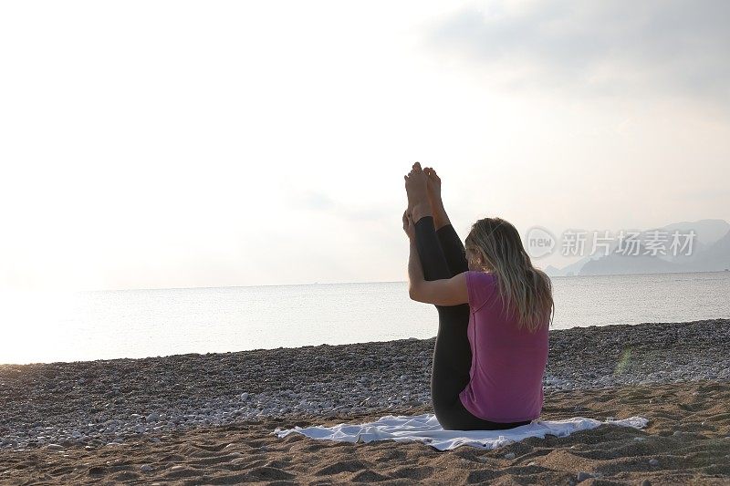 年轻女子在海滩上练习日出瑜伽