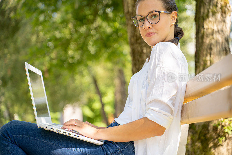 戴眼镜的年轻女子在公园里使用笔记本电脑