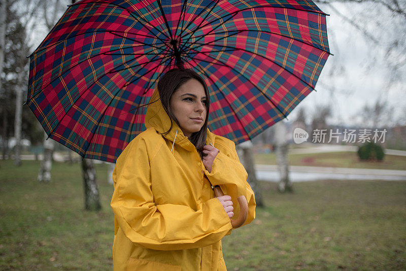 穿着黄色雨衣的年轻女子在公园里度过雨天