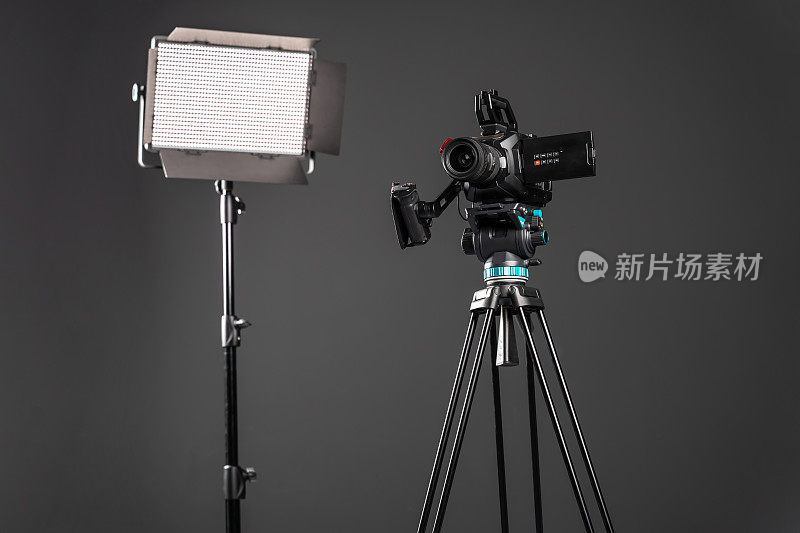 专业影院摄像机在一个摄像机三脚架和一个照明LED面板在黑色背景