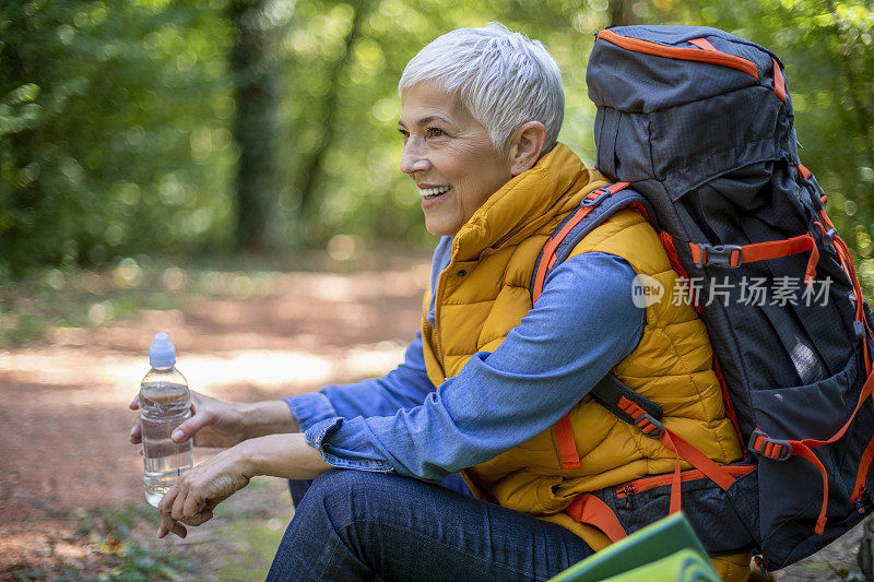 美丽成熟的老年妇女在60岁初的春天森林徒步旅行