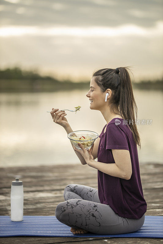 听着音乐，吃着沙拉，坐在湖边码头上的女人