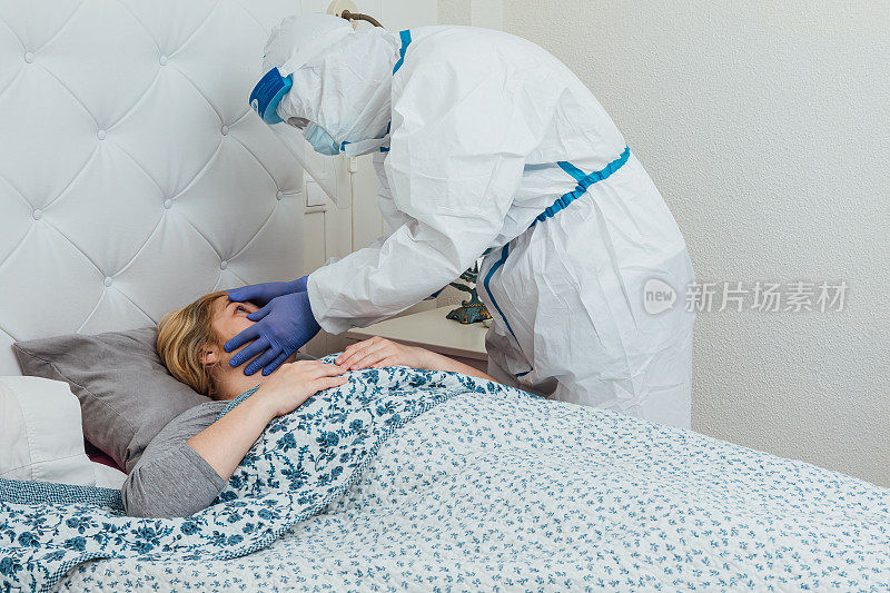 身穿个人防护装备的医生在家里的床上照料一位患有冠状病毒的妇女