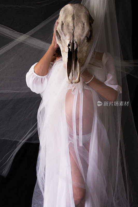 怀孕的加拿大土著妇女，穿着透明的白色长袍，拿着牛头骨遮住脸。