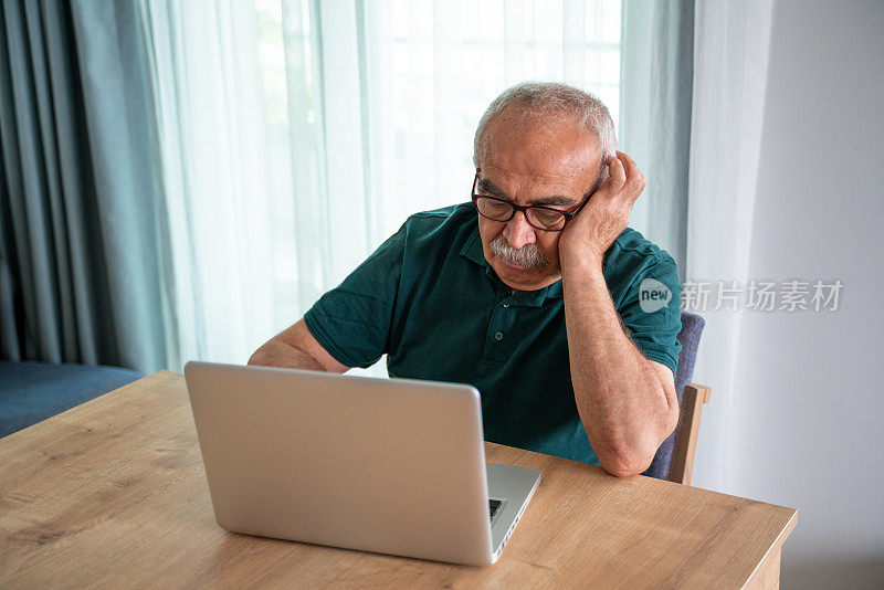 老人坐在客厅的桌子旁用笔记本电脑上网