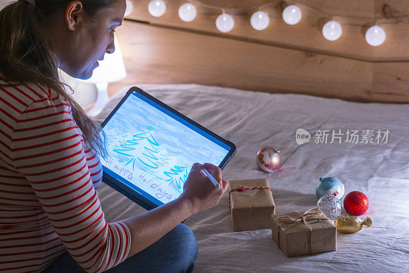 一名女性艺术家用触控笔在数码平板电脑上创作圣诞贺卡，周围是包装好的圣诞礼物。在家里讨论新冠肺炎的现实。新的标准。呆在家里准备寒假。