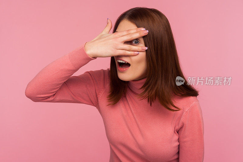 多管闲事的深褐色的女人在粉红色的毛衣间谍通过手指的洞假装闭上眼睛与手，隐藏看秘密