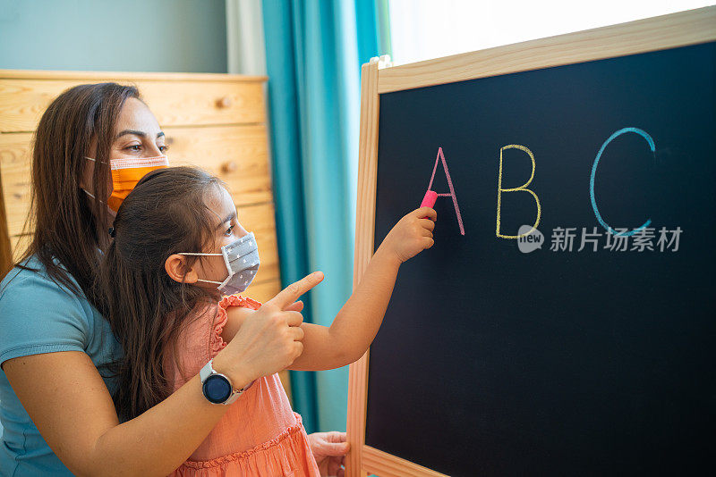 家庭教师和小女生戴着防护面具在家学习黑板上的字母