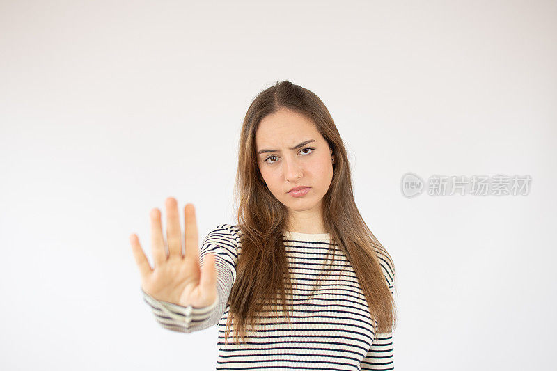 年轻美丽的女孩穿着休闲t恤在白色的背景做停止唱歌与手掌。警告表情与否定和严肃的手势在脸上。