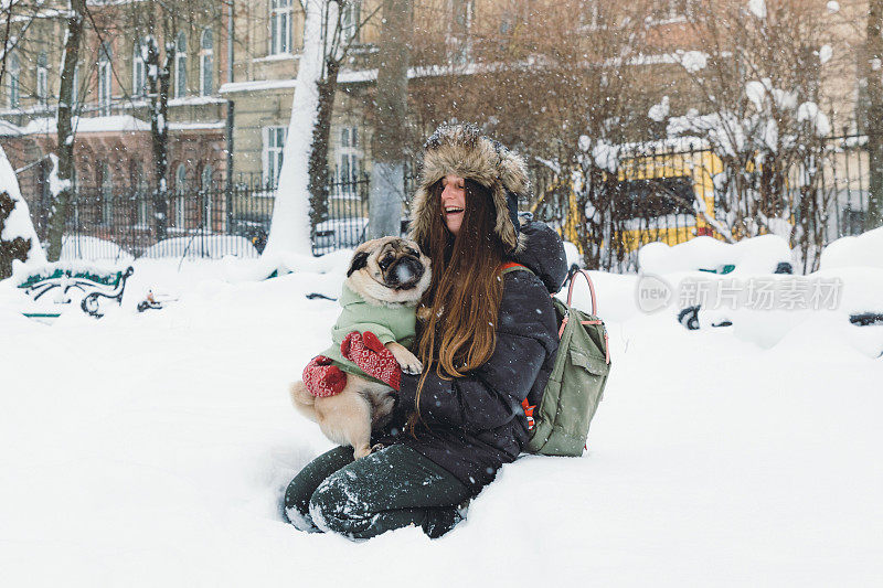 快乐的年轻女子背包享受第一雪在公园散步与小可爱的狗