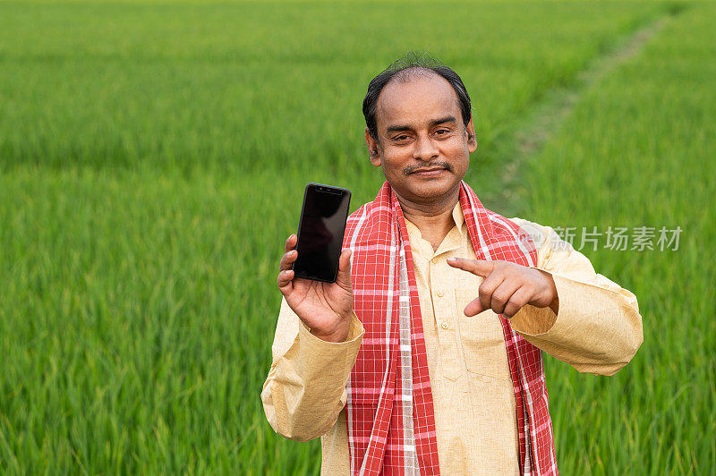 印度农民在绿色农田里展示手机