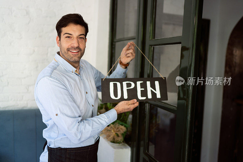 兴高采烈的餐馆老板在门上挂着敞开的牌子