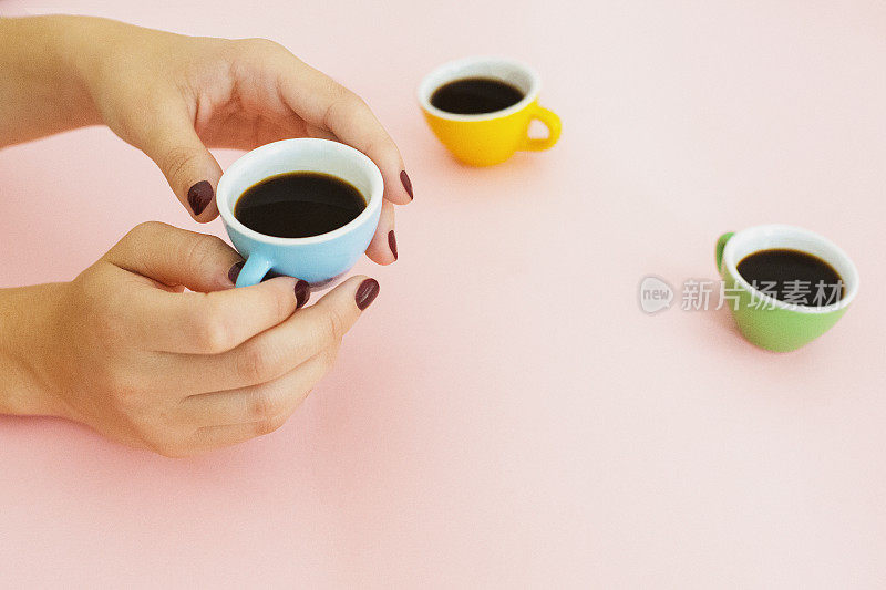 手拿一个粉红色背景的小咖啡杯