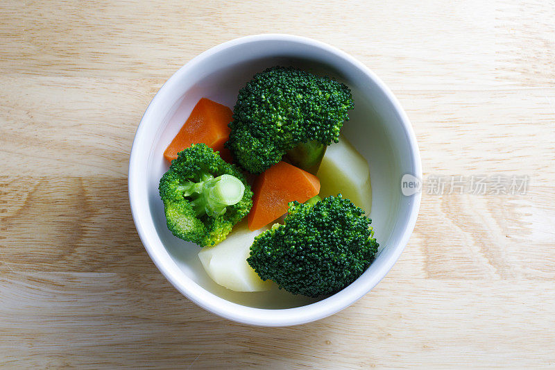 用白色碗盛着土豆、花椰菜和胡萝卜的蔬菜沙拉。