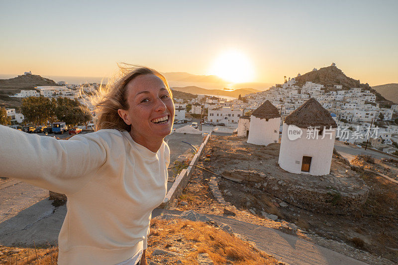 年轻女子在日落时自拍在希腊群岛，有趣的风假期