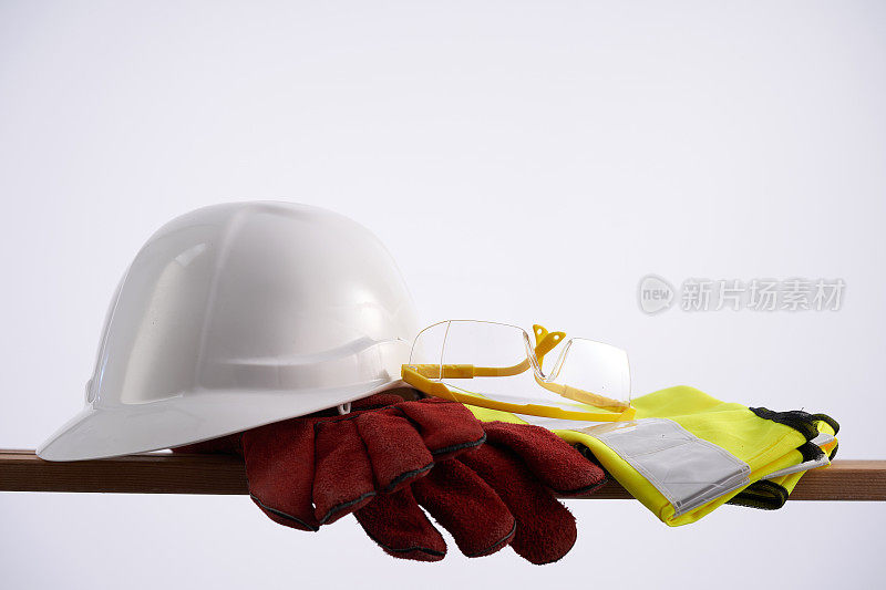黄色塑料安全帽、眼镜、反光背心和防护手套放在木板上。安全劳动的概念