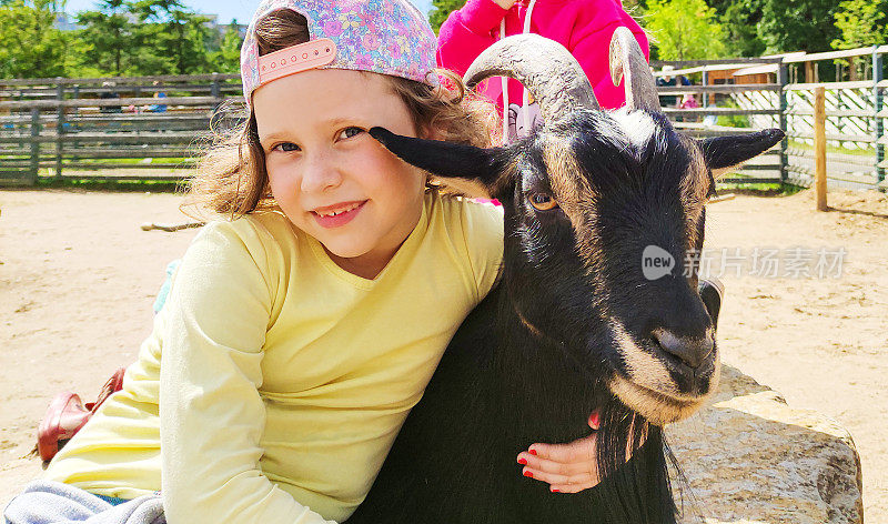 一个7岁的白人女孩，微笑着看着镜头，抱着一只黑色的山羊。