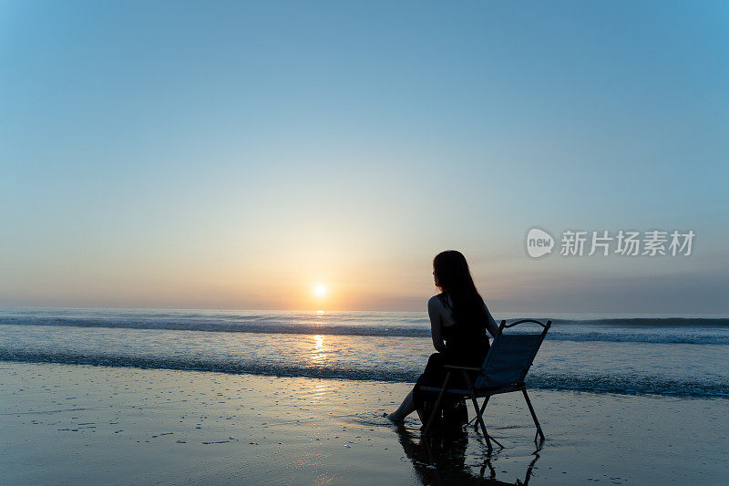 一位年轻女子坐在沙滩上的椅子上看日出