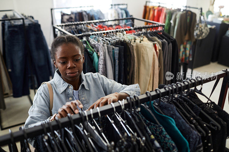 黑人年轻女子在旧货店购物时正在看衣服