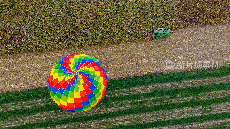 鸟瞰图热气球站在农业领域旁边的玉米田，联合收割机种植玉米植物