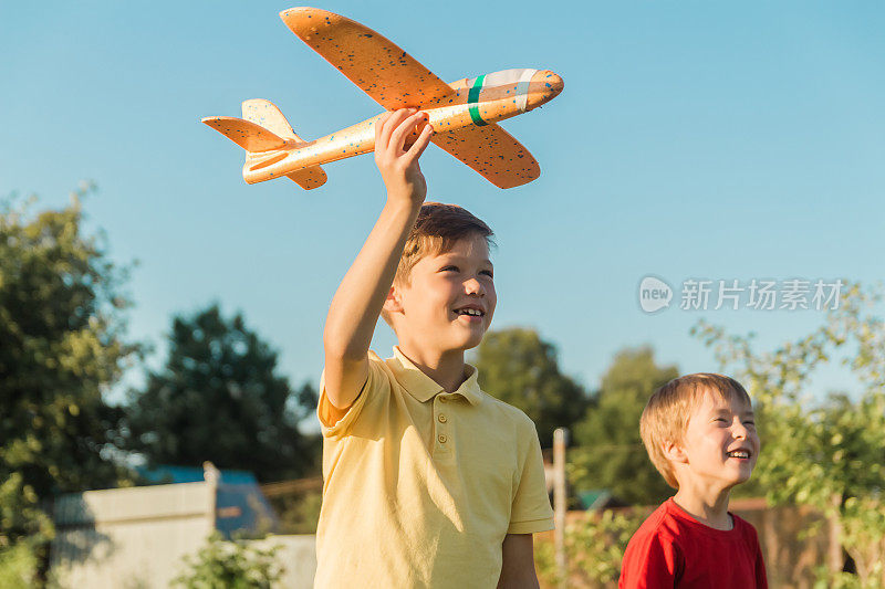 两个男孩在夏天带着玩具飞机跑过田野。快乐的孩子们在公园里跑来跑去，在户外玩玩具飞机。兄弟们梦想着飞翔。无忧无虑的孩子玩耍。幸福的家庭