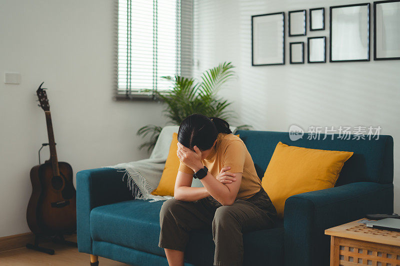 一名亚洲妇女正坐在家里客厅的沙发上饱受头痛之苦。