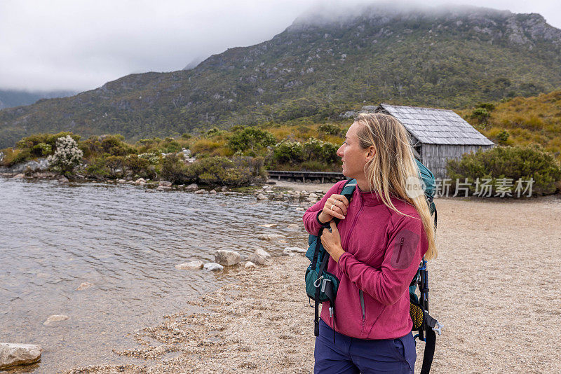 绿洲山:一个女徒步旅行者调整她的背包，暂停在雄伟的山峰湖