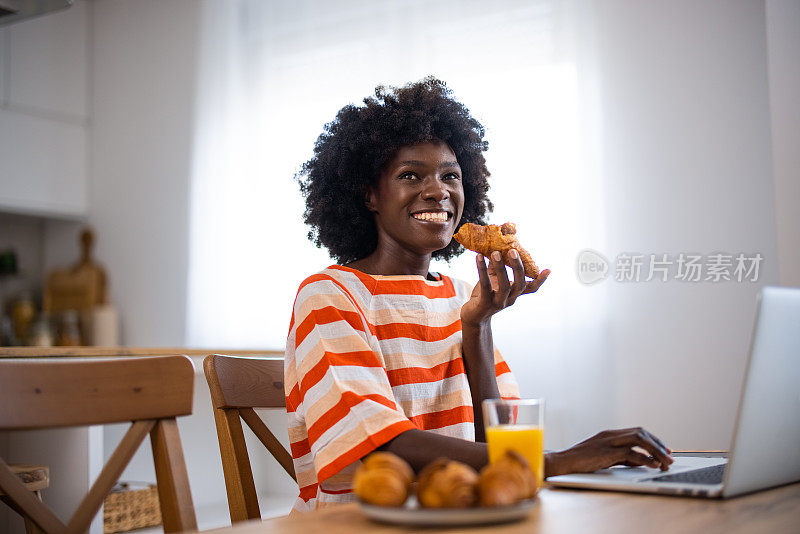 一名非洲裔美国年轻女子边吃午饭边用笔记本电脑