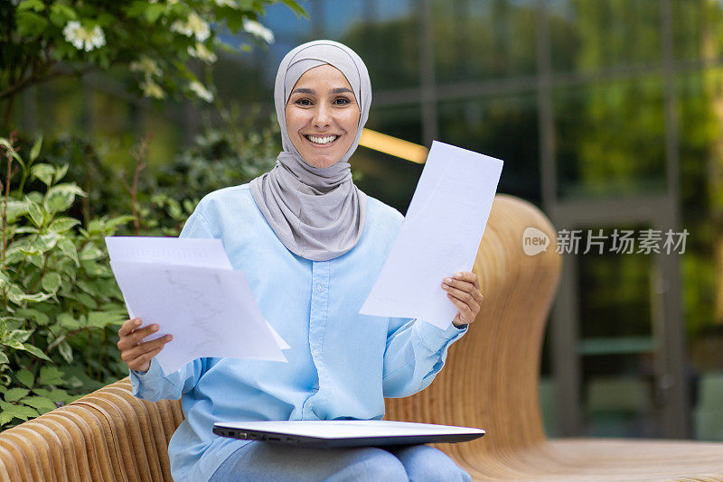 自信的穆斯林女商人带着文件坐在户外微笑