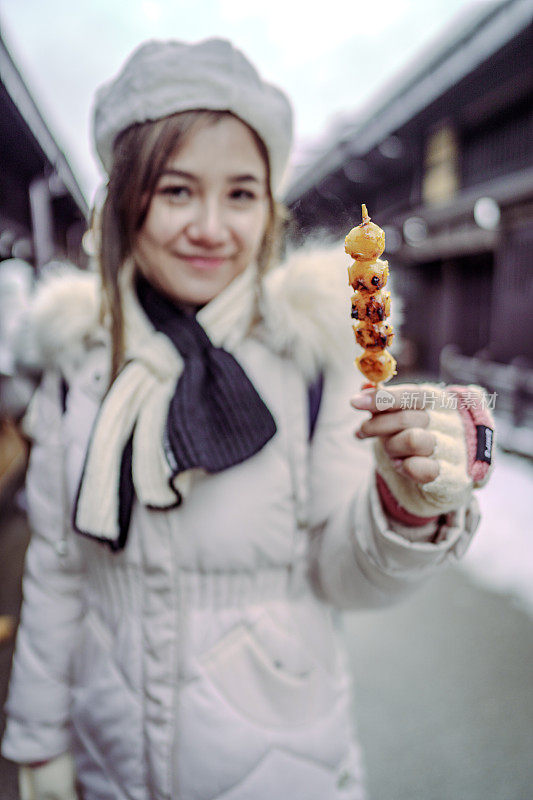 美丽的女游客在雪天的日本之旅中品尝日本街头小吃
