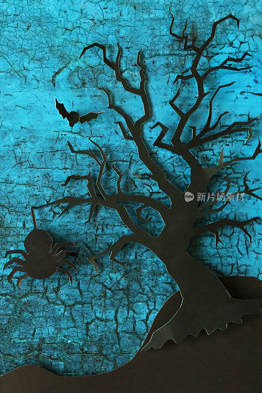 图片万圣节之夜设计海报场景，巨大蜘蛛的剪影剪影形状悬挂在落叶树上，树枝光秃秃的，蝙蝠在破碎的蓝色背景上