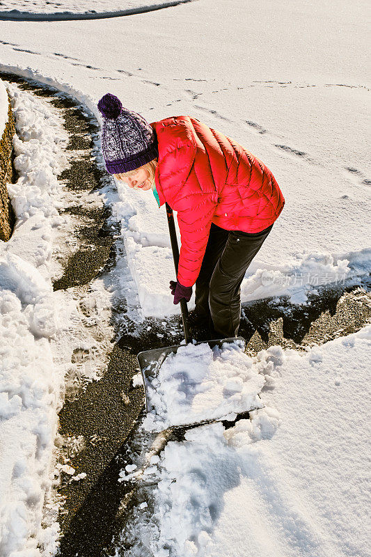 一个女人在车道上用雪铲