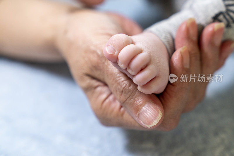 奶奶抱着孩子的脚。母亲的手和孩子的脚。家庭的概念