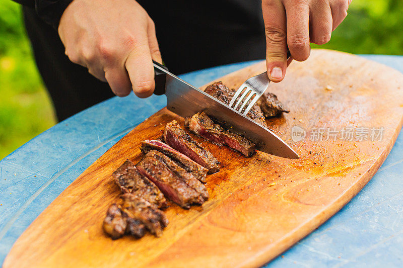 新鲜牛排。满足户外经验。晚餐在后院。红肉。准备食物的过程。小牛肉。美味的小吃。户外用餐。烤食物。用刀切肉