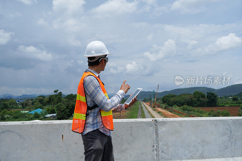 一名亚洲工程师在外面用电子平板检查修建一条高速铁路。