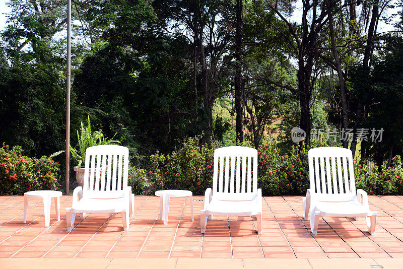 游泳池，白色的椅子和自然花园的背景