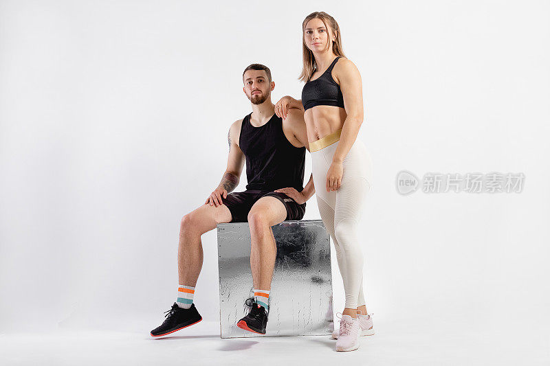 摄影棚中男女合影。健身理念，锻炼肌肉。专业运动员，适合摄影。两个人一边运动一边坐在立方体上