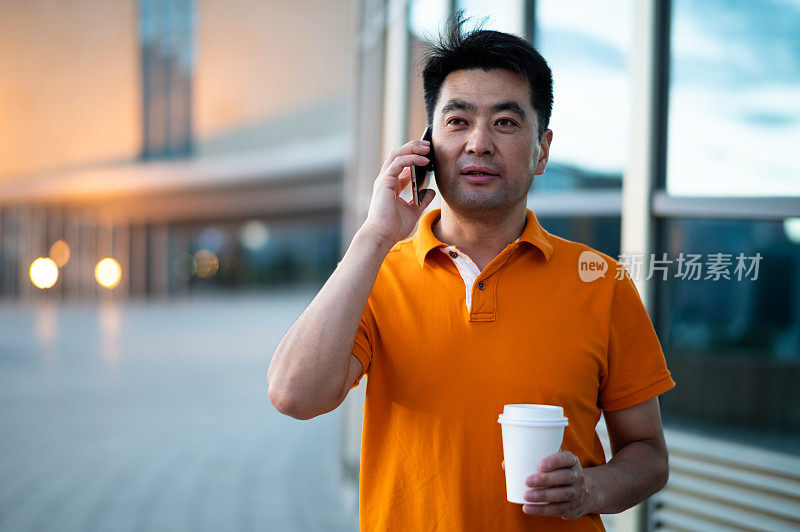 亚洲中年男子手持咖啡杯，在城市街道上使用智能手机